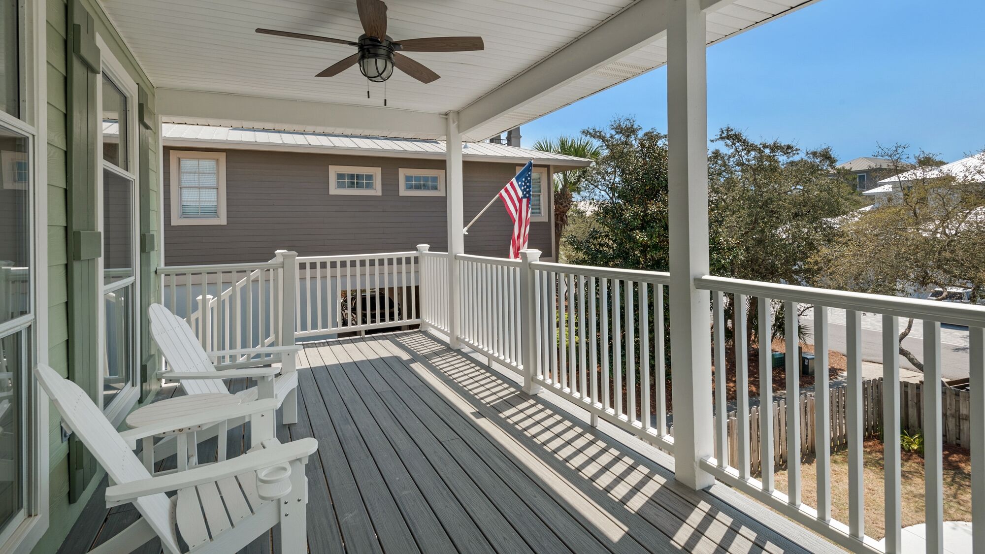 A covered porch with white railings, a ceiling fan, and an American flag.