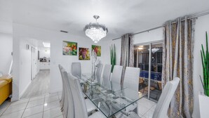 A modern dining area with a glass-top table, white chairs, and a chandelier.