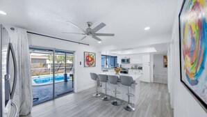 A modern kitchen with a central island, bar stools, and a ceiling fan.