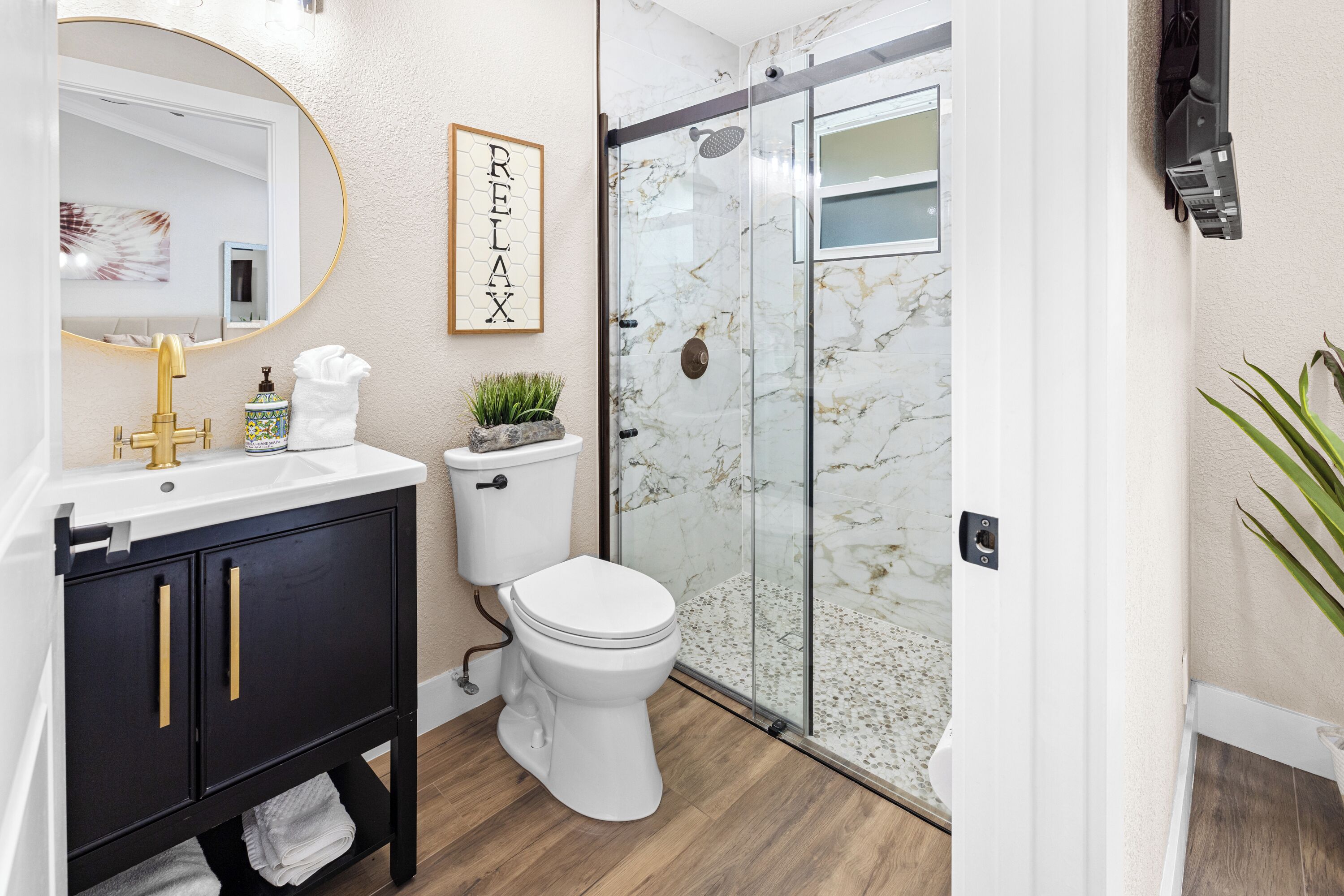 Et moderne badeværelse med et hvidt toilet, en sort kommode med guldgreb, en brusekabine i glas og et skilt med ordet 'RELAX' på væggen.