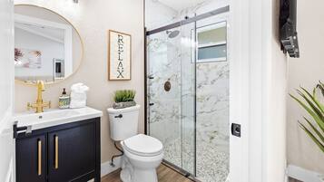 Et moderne badeværelse med et hvidt toilet, en sort kommode med guldgreb, en brusekabine i glas og et skilt med ordet 'RELAX' på væggen.