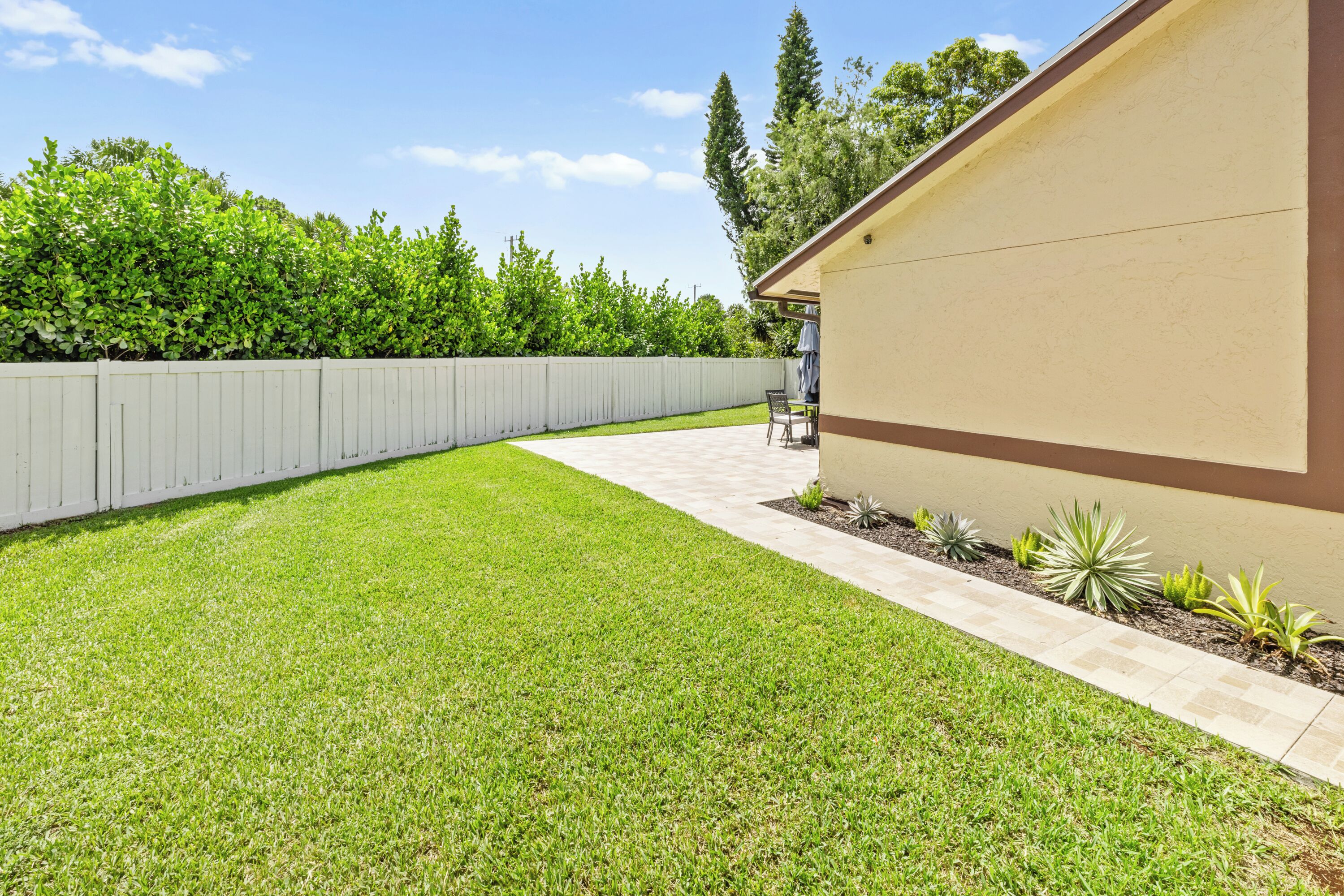 A well-maintained backyard with a patio, a white fence, and various plants.