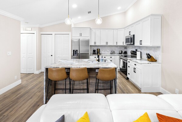 A modern kitchen with white cabinets, a marble island, and bar stools.