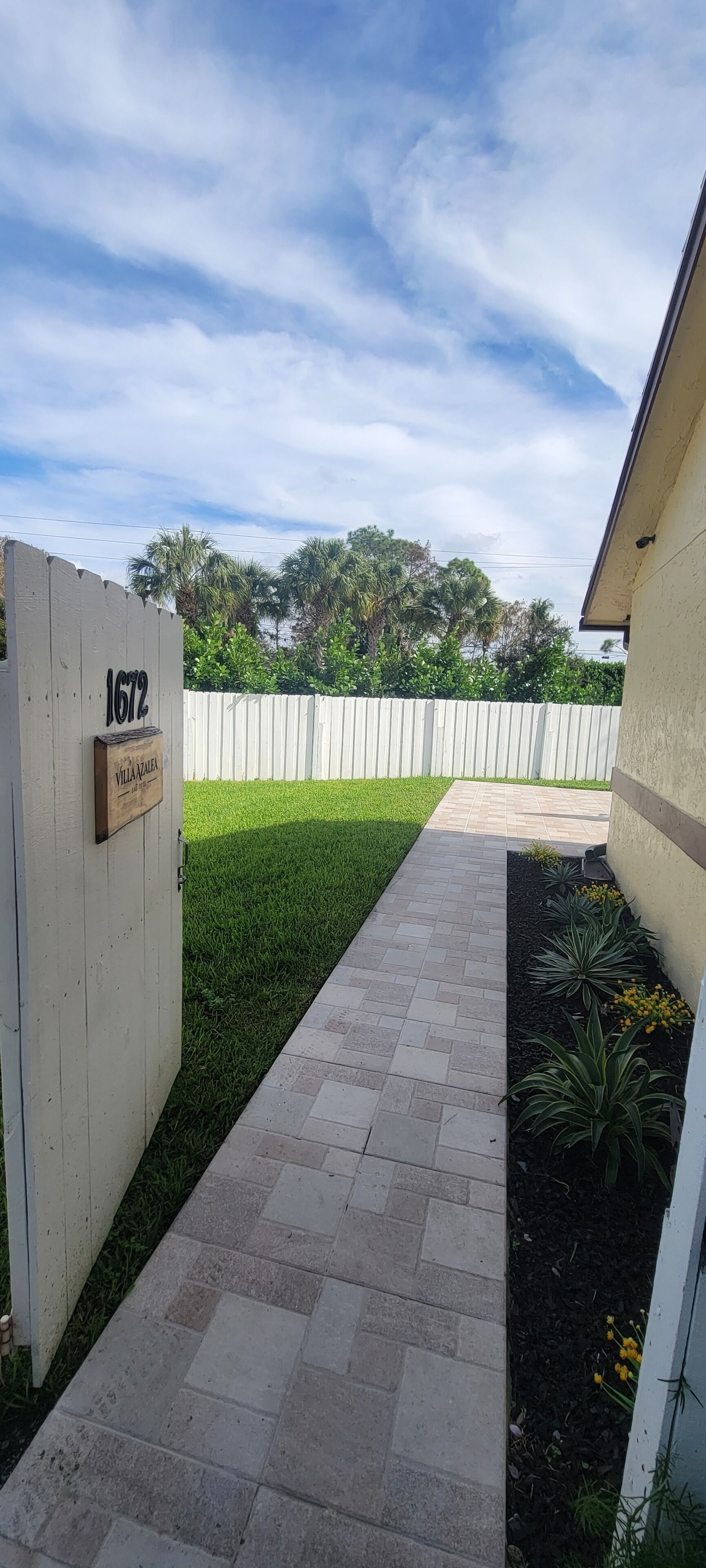 A paved pathway leading to a gated entrance with a sign reading "1672" and "VILLAZA".