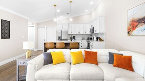 Un salon moderne avec un canapé d’angle blanc, une petite table d’appoint et une plante décorative.