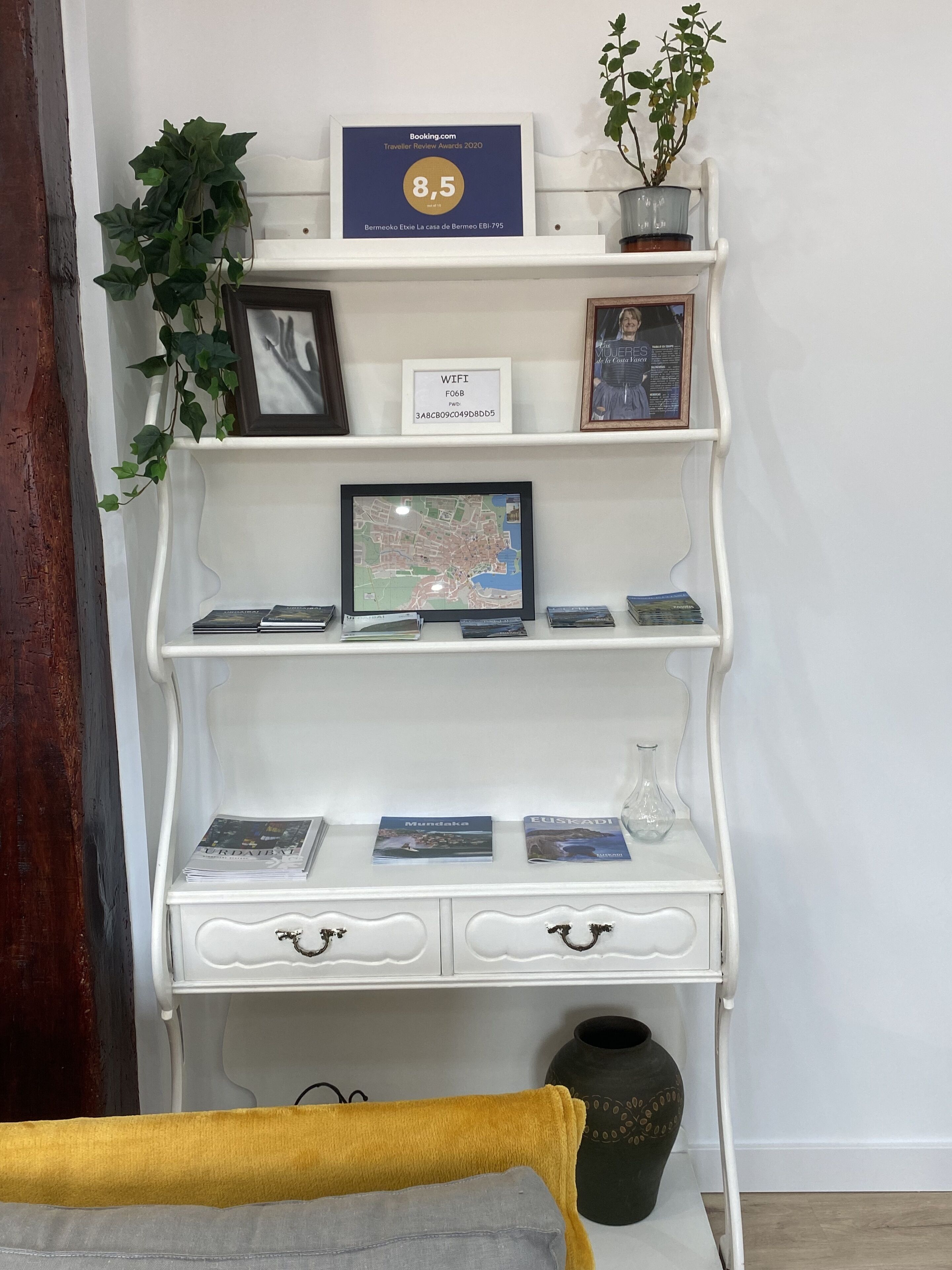 A white shelf with a framed map, a framed certificate, a potted plant, and a vase.