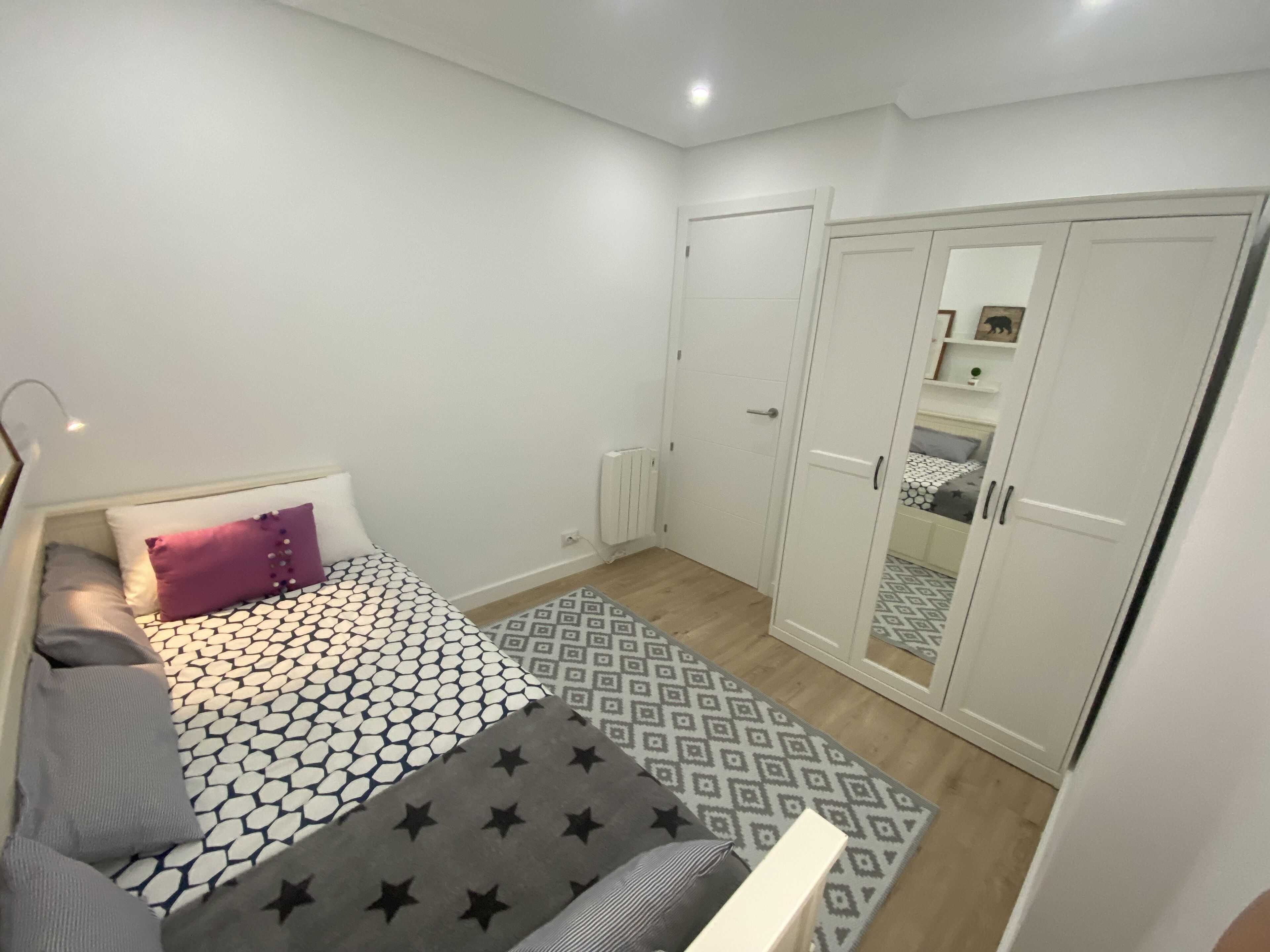 Un dormitorio con cama, armario y espejo.