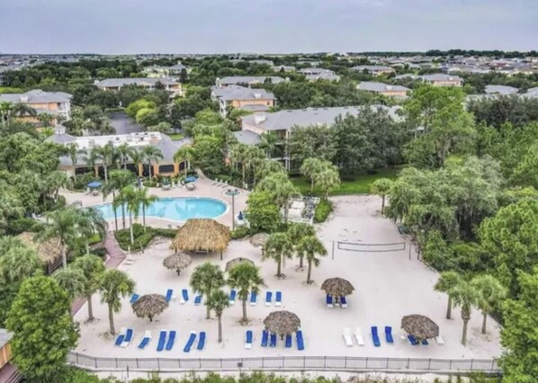 A resort with a swimming pool, lounge chairs, and palm trees.