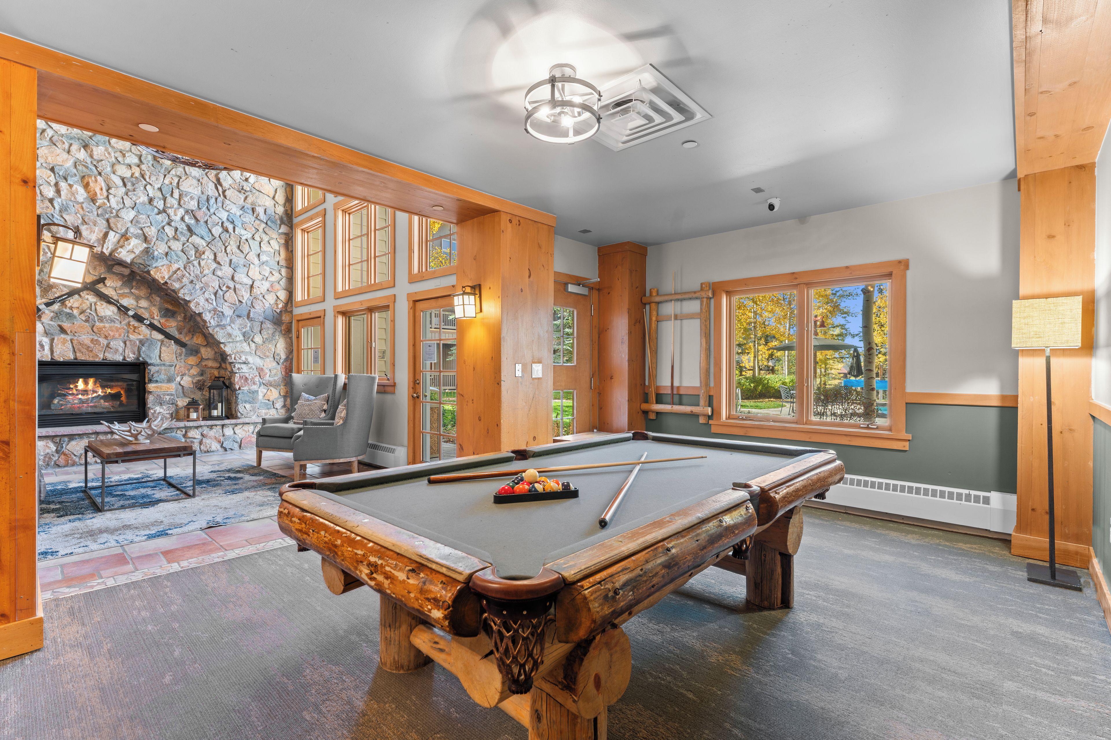 A pool table in a room with stone walls, a fireplace, and large windows.
