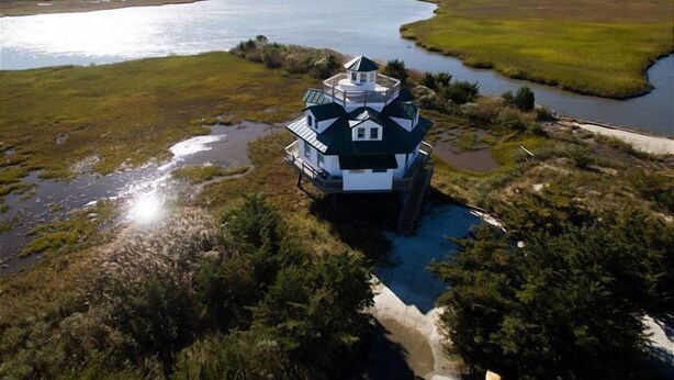 Een huis met een groen dak en witte muren, omringd door een moerachtig landschap en een rivier.