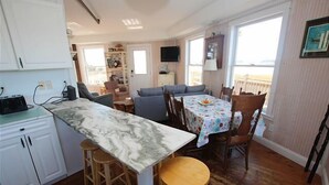 Een kleine keuken met een marmeren aanrecht, houten krukken, een eettafel met stoelen en uitzicht op de omgeving.