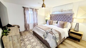 A bedroom with a large bed, a ceiling fan, a nightstand with a lamp, and a window with curtains. - POSHPADZ -OceanView Villa-Resort Complex, Penthouse, Sleeps 4, Walk to Beach (Jupiter)