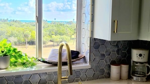 A kitchen with a view of a vineyard, a sink with a towel, and a coffee maker. - POSHPADZ -OceanView Villa-Resort Complex, Penthouse, Sleeps 4, Walk to Beach (Jupiter)