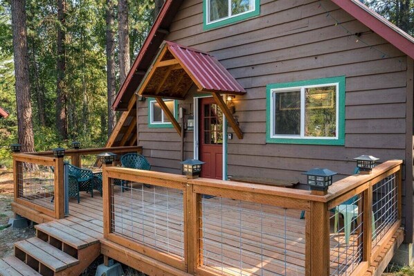 Une cabane en bois dotée d’une terrasse, d’une porte rouge et d’un petit porche surmonté d’un toit rouge.