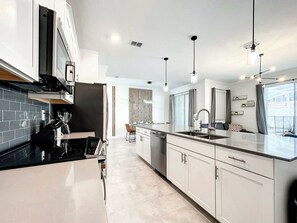 Une cuisine moderne dotée d’un îlot central, d’appareils électroménagers en acier inoxydable et de luminaires suspendus.