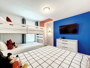 A bunk bed room with a television, dresser, and a window with blinds.