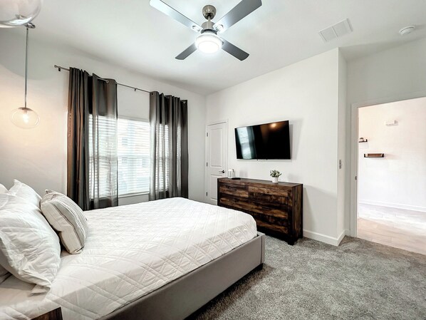 A bedroom with a bed, a dresser, a television, and a ceiling fan.