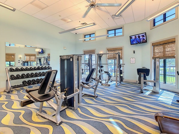 A gym with exercise equipment, a television, and large windows.