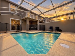Une piscine intérieure avec un toit en verre offrant une vue dégagée sur le ciel, entourée d’une terrasse couverte aménagée avec des sièges.