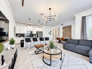 Un salon moderne avec un canapé gris, une table basse ronde et un coin repas comprenant une table et des chaises en bois.