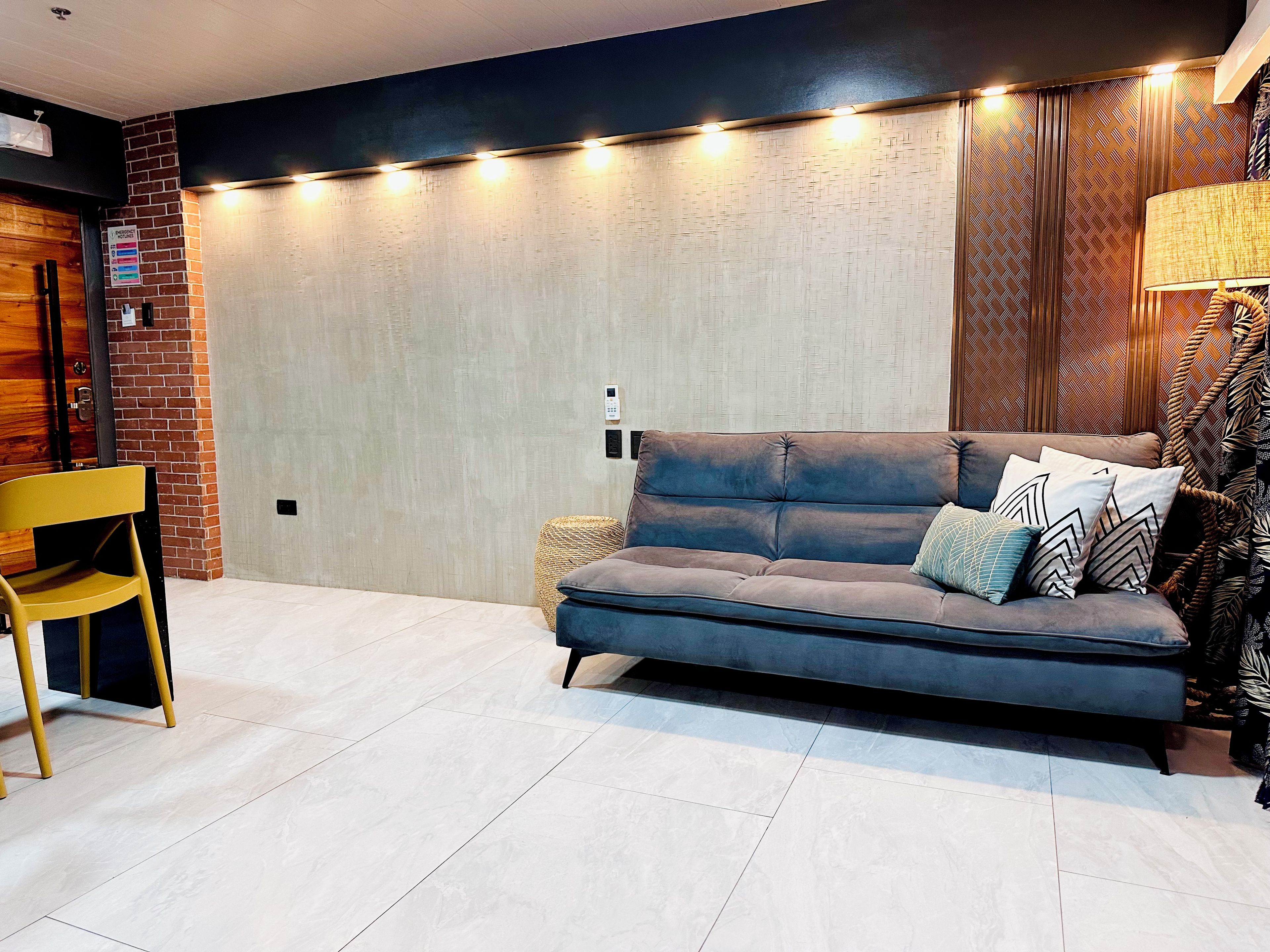 A modern living room with a sofa, a chair, a lamp, and a patterned wall.