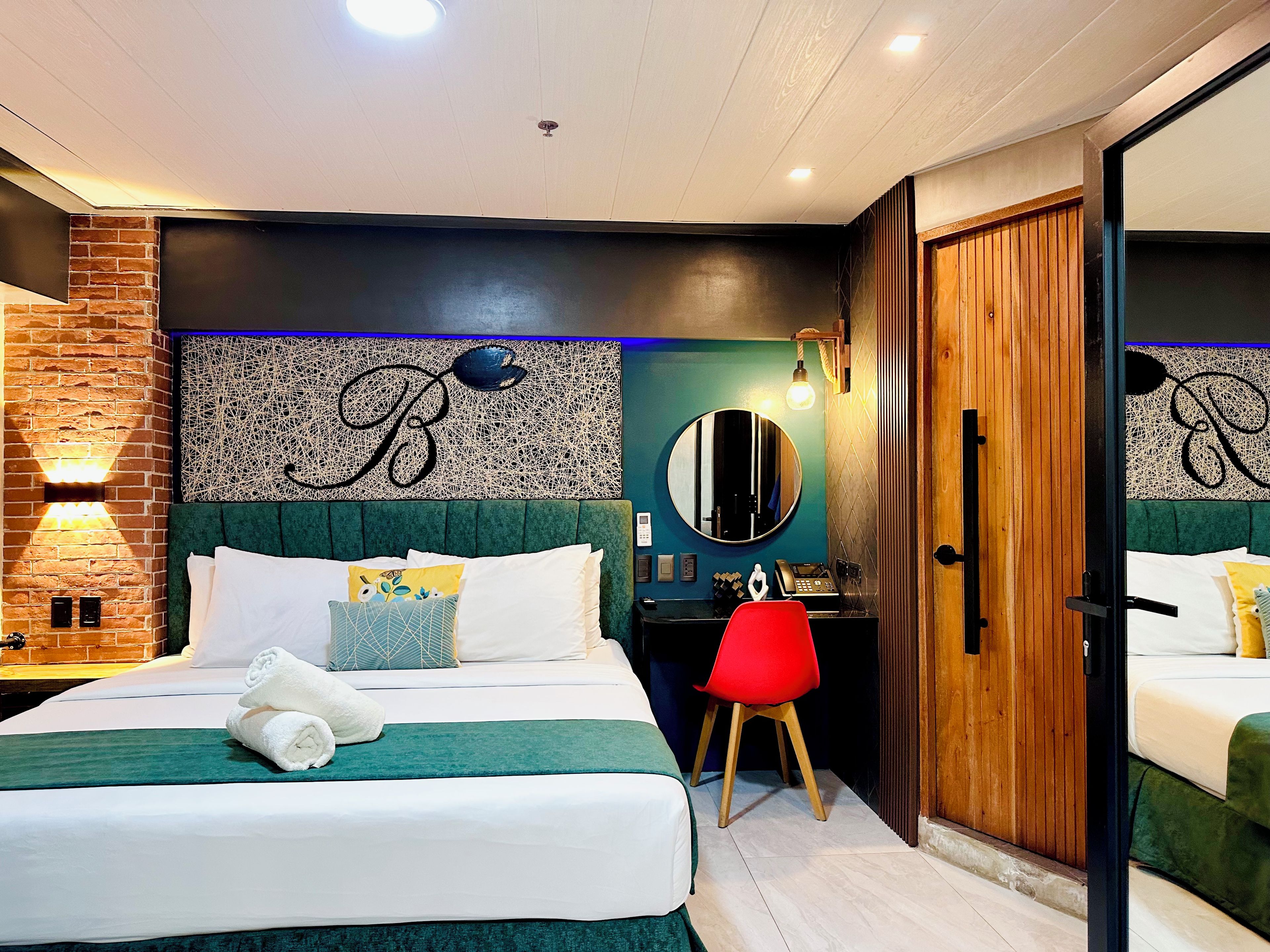 A hotel room with a bed, a desk, a chair, a mirror, and a wardrobe.