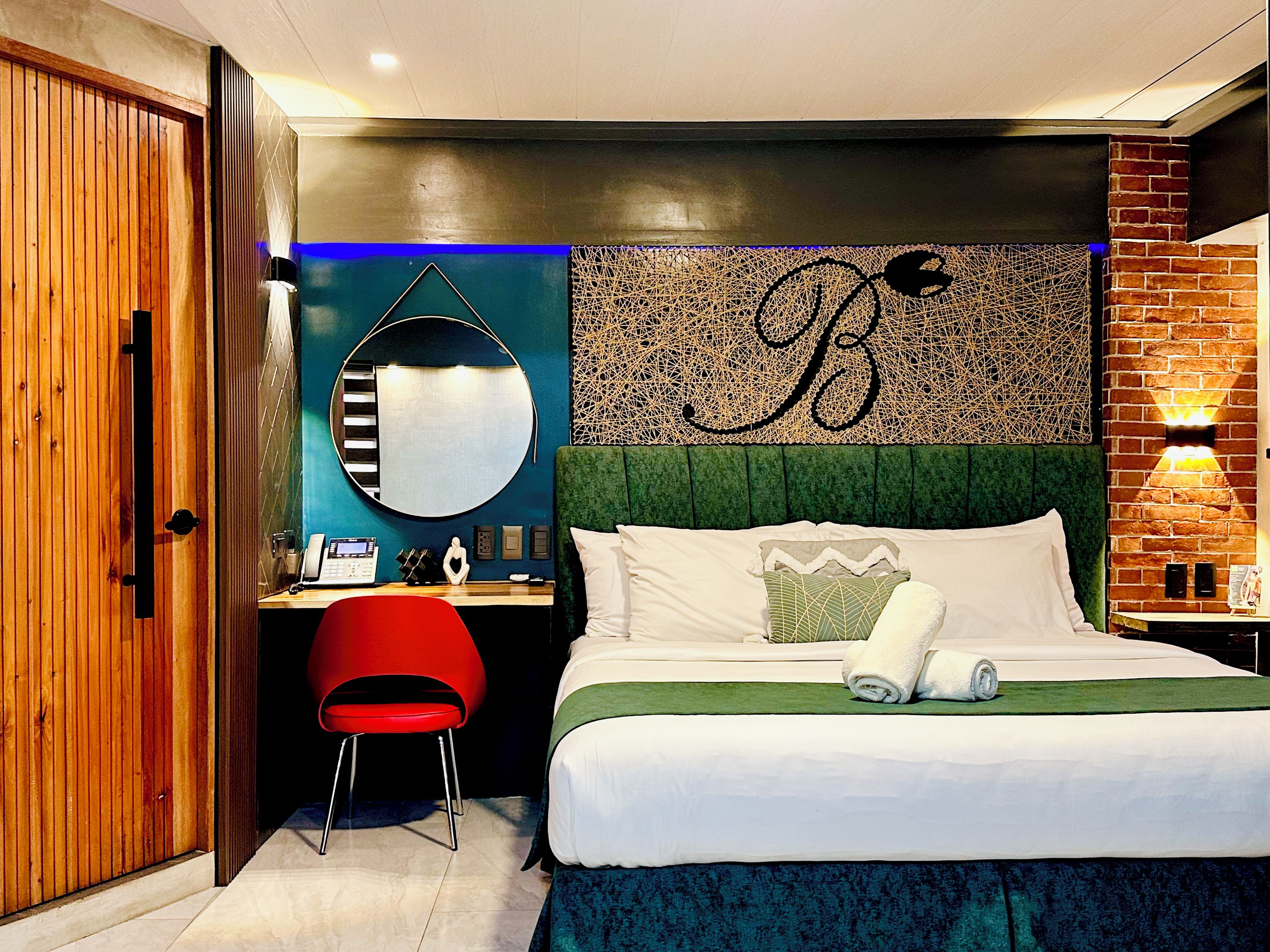 Une chambre d’hôtel comprenant un lit, un bureau, une chaise, un miroir et un mur décoré avec un motif en forme de lettres.