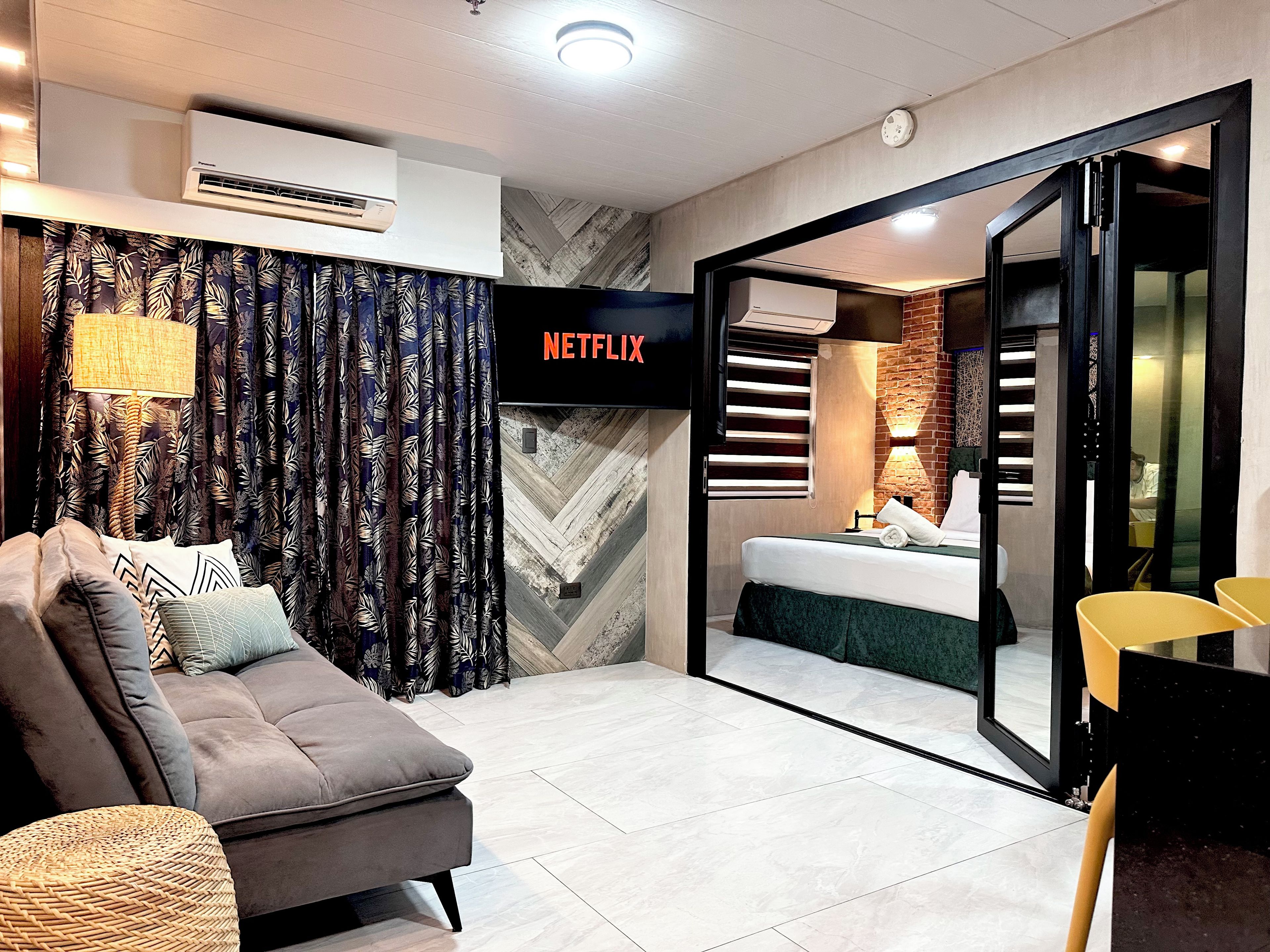 A modern hotel room with a sofa, a flat-screen TV, a bed, and a bathroom visible through an open door.