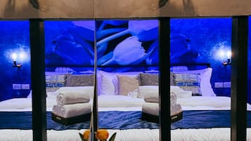 A room with a bed, towels, a vase with flowers, and a view of an ice cave through a large window.