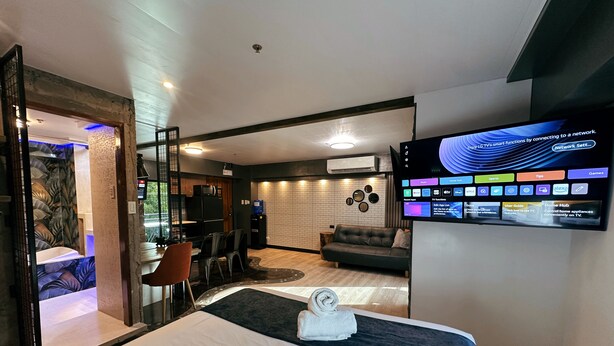 A modern hotel room with a large bed, a TV mounted on the wall, a dining area, and a living space. - Blue Tulip (Lapu-Lapu)
