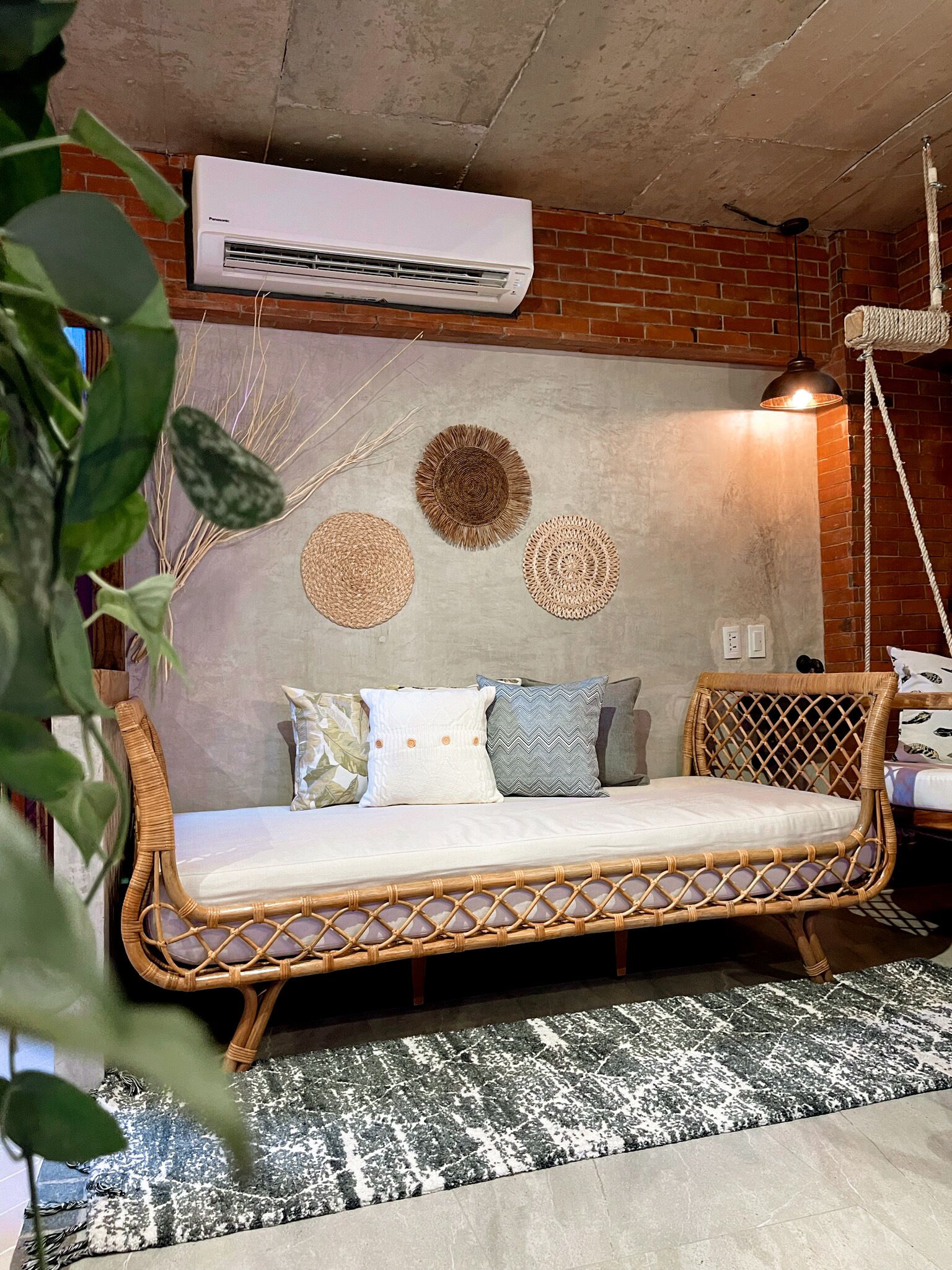 A wicker sofa bed with a cushion, a woven wall decoration, and a hanging light fixture.