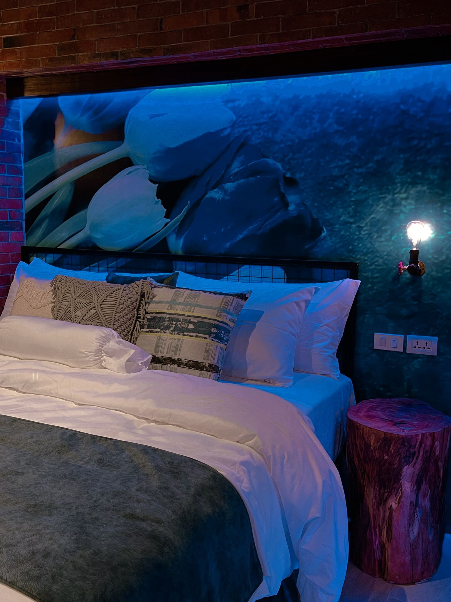 A bedroom with a bed, pillows, a nightstand, and a wall-mounted light fixture.
