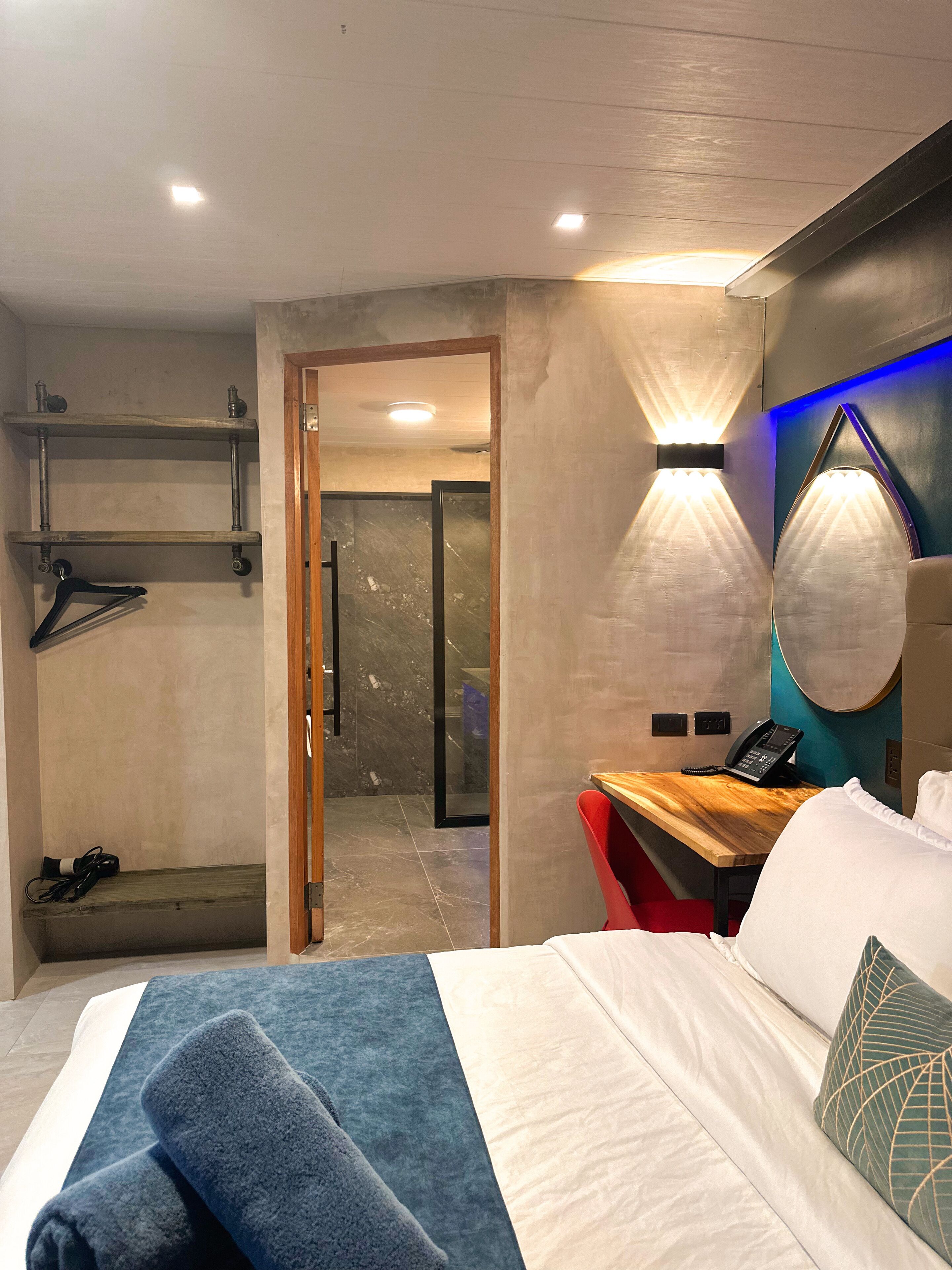 Una habitación de hotel con una cama, un escritorio con teléfono, un espejo y una puerta que da a un baño.