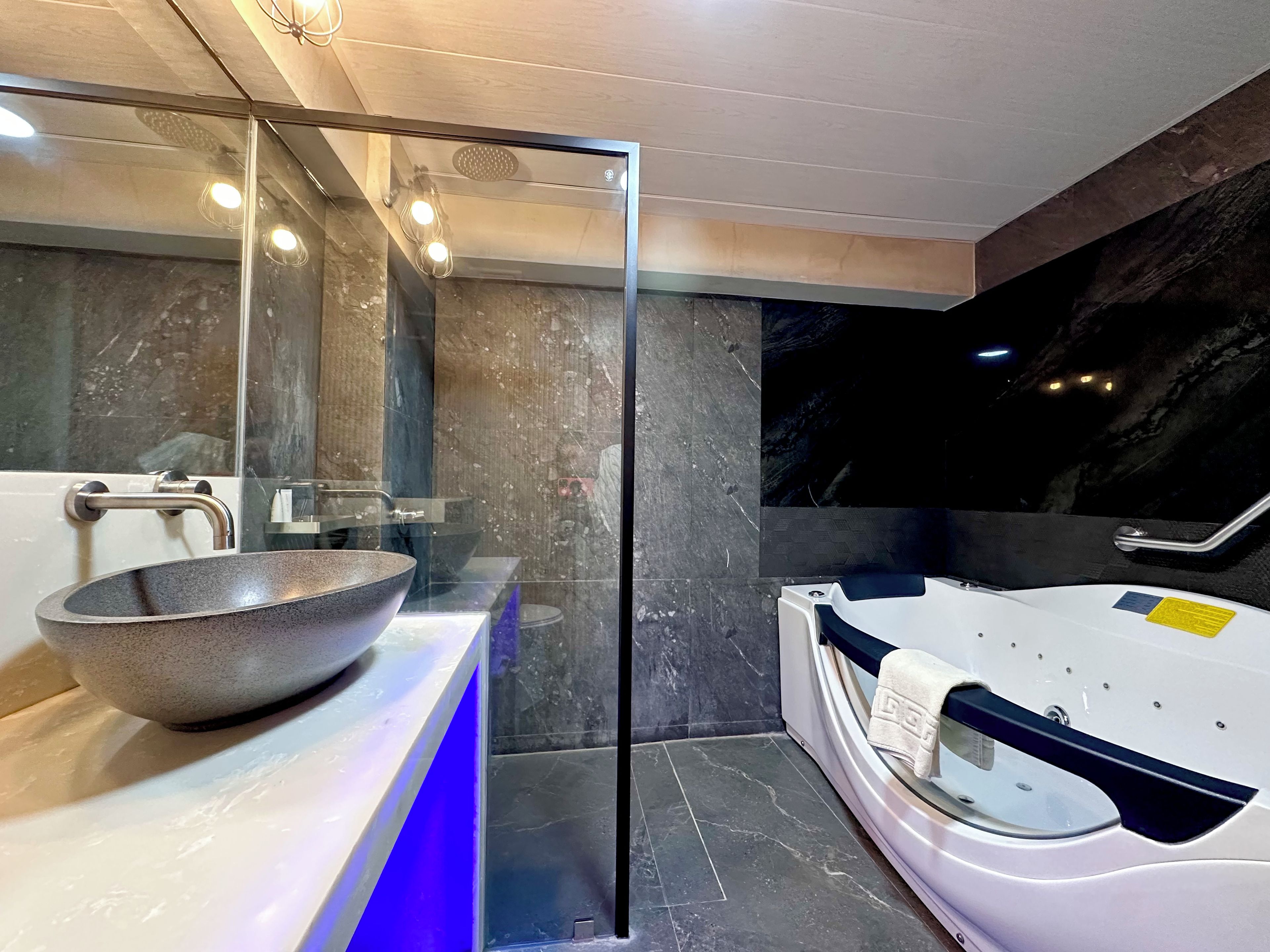 Un baño moderno con cabina de ducha de vidrio, un lavamanos grande tipo recipiente y una bañera blanca.