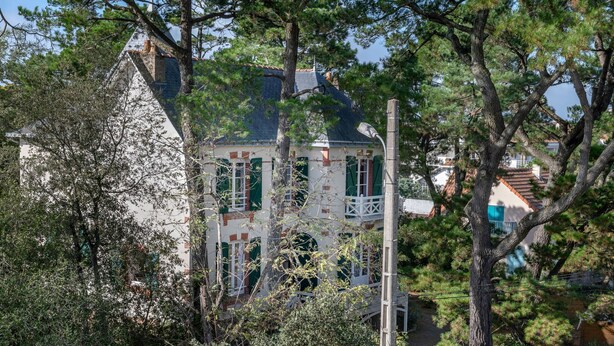 A traditional house with a steep roof, surrounded by trees and a clear sky.