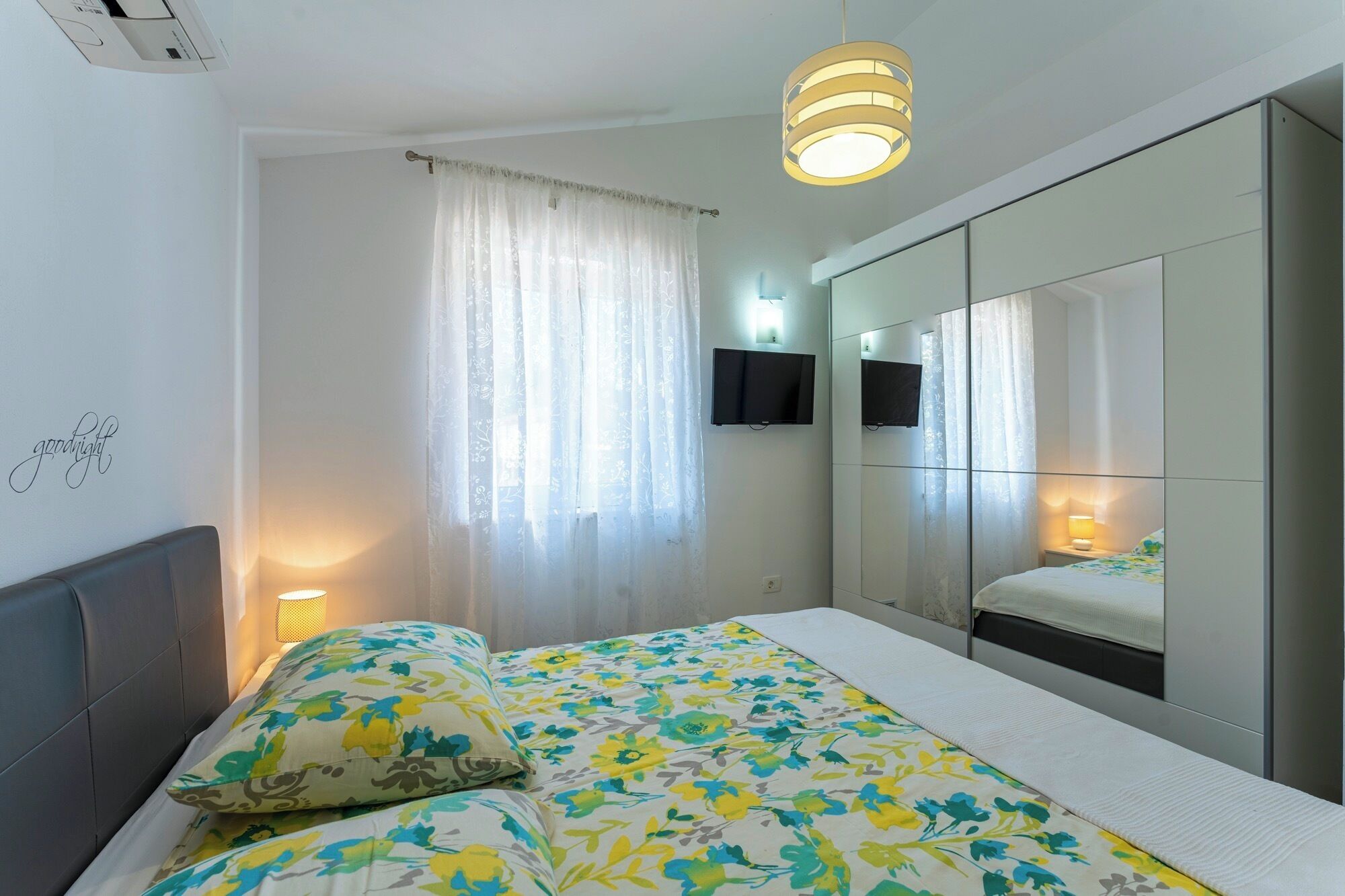 Une chambre à coucher avec un lit, une lampe de chevet, une télévision et un miroir.