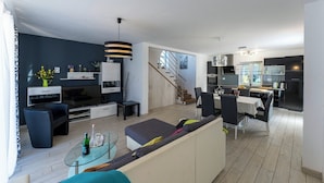 Un salon moderne comprenant un canapé, un téléviseur et un coin repas avec des chaises et une table.