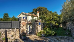 Une maison avec une façade en pierre, un toit en tuiles et une entrée fermée par un portail.