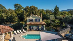Une maison à deux étages avec une piscine, un espace extérieur aménagé et un mur en pierre.