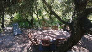 An outdoor dining area with a round wooden table and chairs, surrounded by trees and plants.