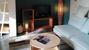 A modern living room with a teal accent wall, a white sofa, a round coffee table, and a flat-screen TV on a wooden stand.