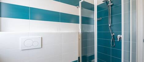 A bathroom with a glass shower enclosure, white and teal tiles, and a visible light switch.