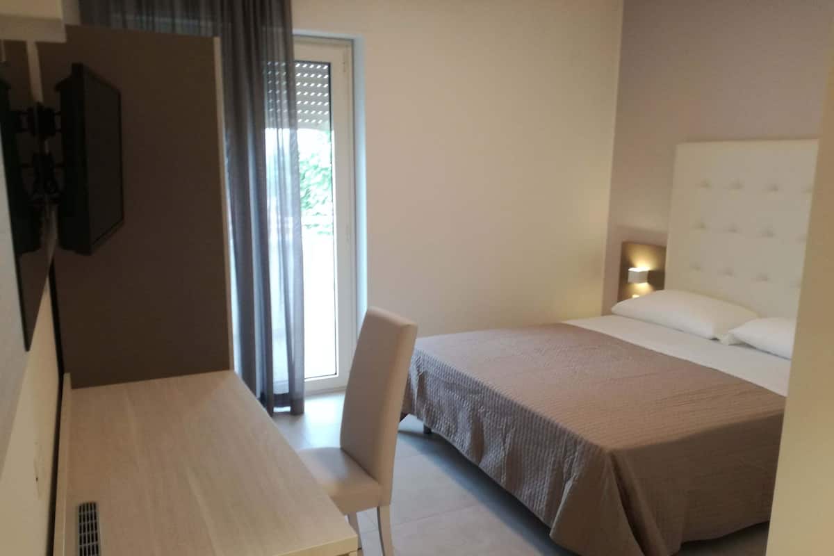 Ein Hotelzimmer mit Bett, Schreibtisch, Stuhl, Fernseher und einem Fenster mit Vorhängen.