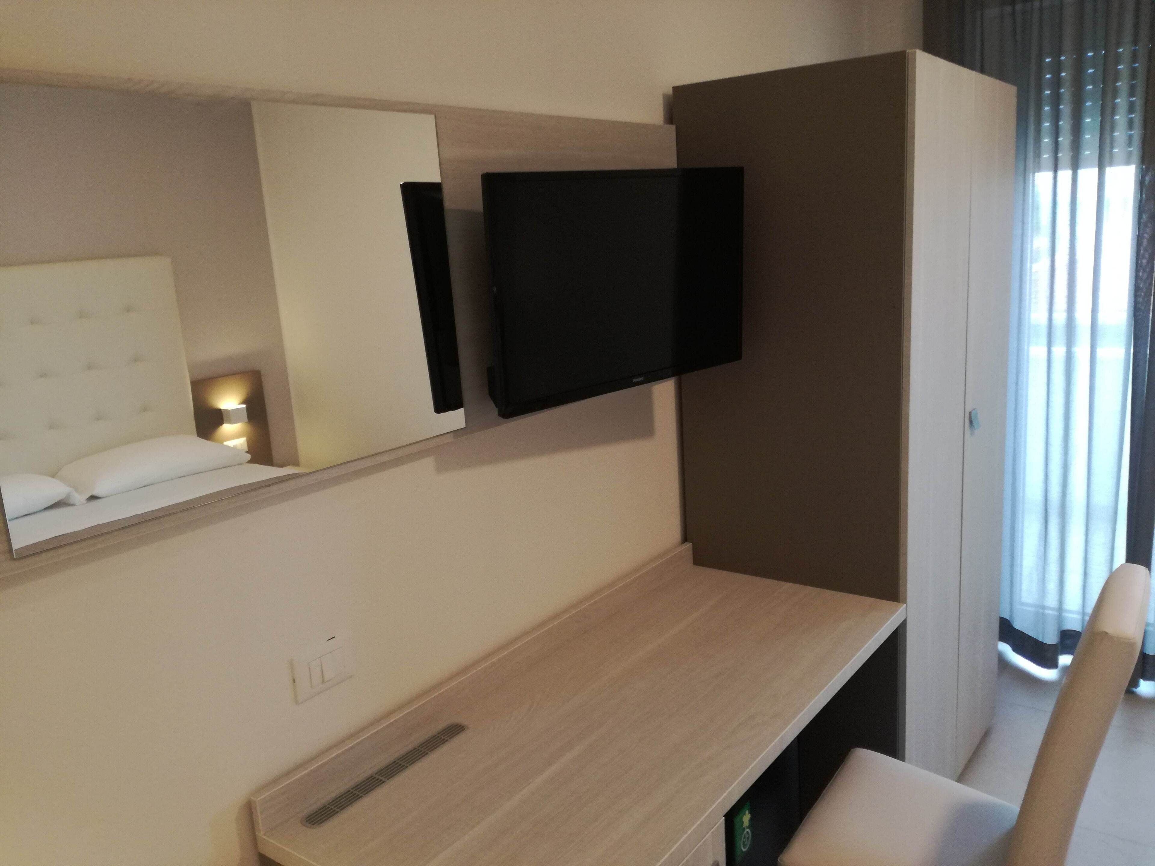 Una habitación de hotel moderna con una cama, un televisor de pantalla plana en la pared, un escritorio de madera y una silla.