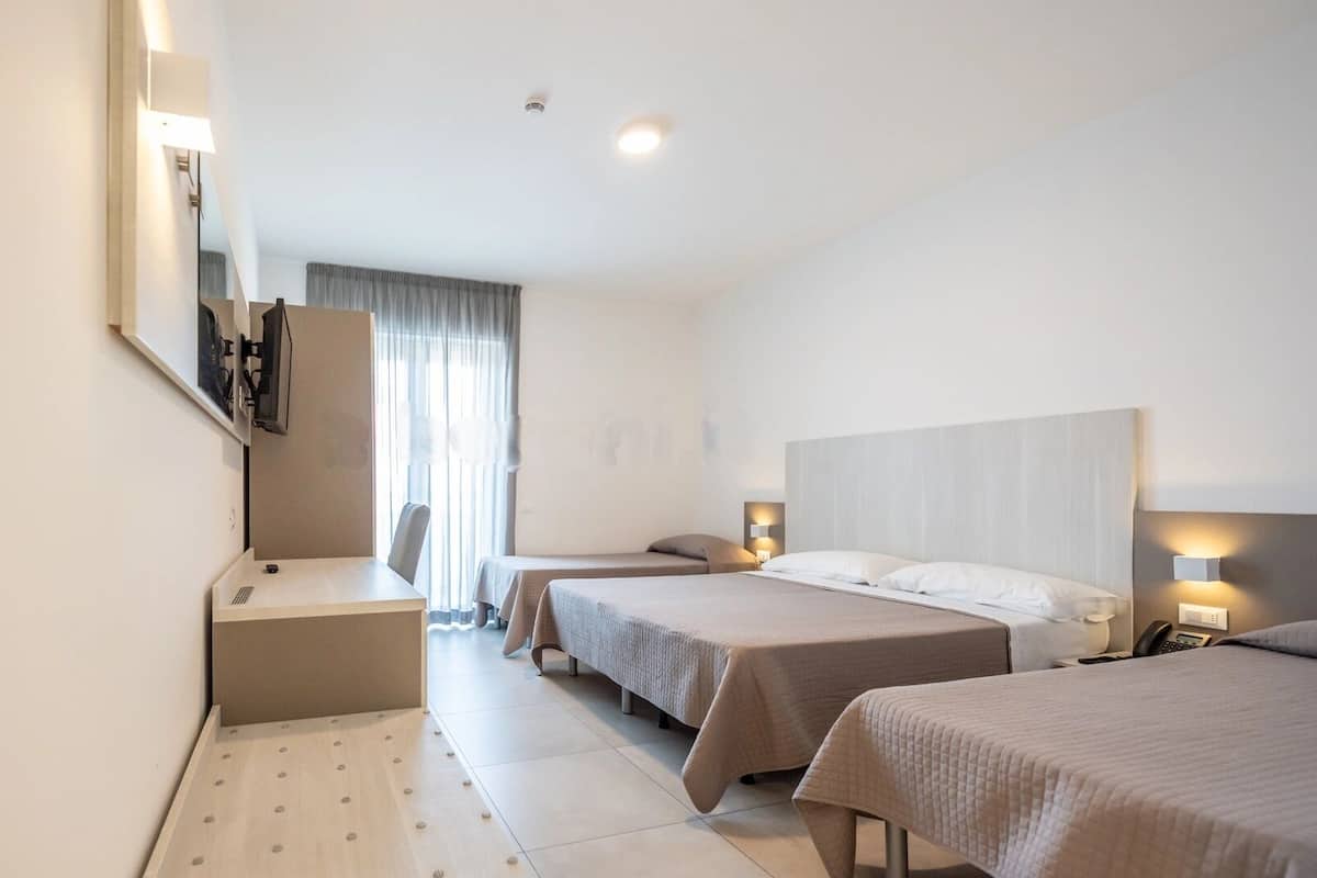 Ein Hotelzimmer mit zwei Einzelbetten, einem Schreibtisch, einem Stuhl, einem Spiegel und einem Fenster mit Vorhängen.