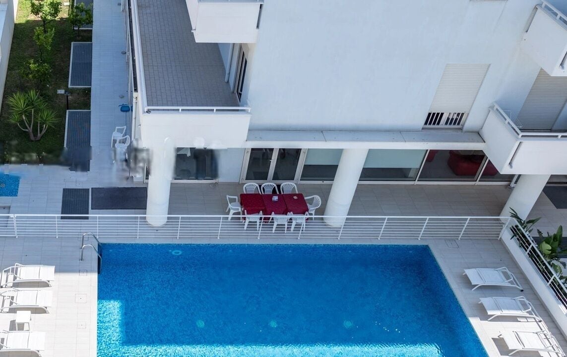 A rooftop pool with a table and chairs, surrounded by a white building with balconies.