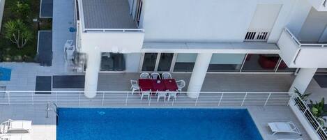 A rooftop pool with a table and chairs, surrounded by a white building with balconies.