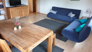 Olohuoneessa on puinen pöytä, sininen sohva ja televisio, joka on sijoitettu puiseen kaappiin.