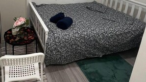 Una habitación pequeña y ordenada con una cama, una silla y una mesita con flores.