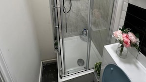 Un baño pequeño con cabina de ducha de vidrio, un lavamanos blanco y un inodoro.